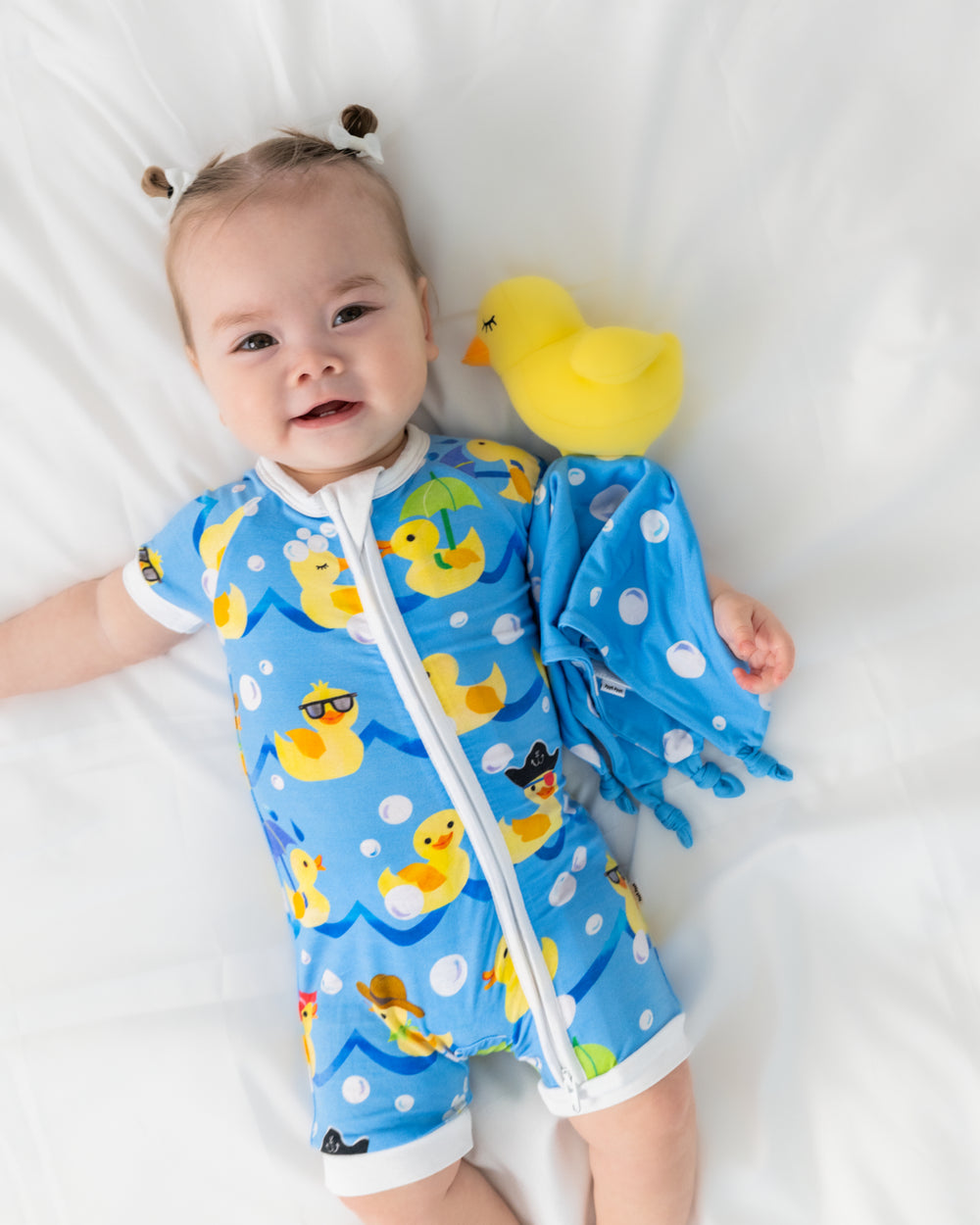 Baby wearing the Splish Splash zippy holding the Bubbles the Rubber Ducky Sleepyhead Lovey
