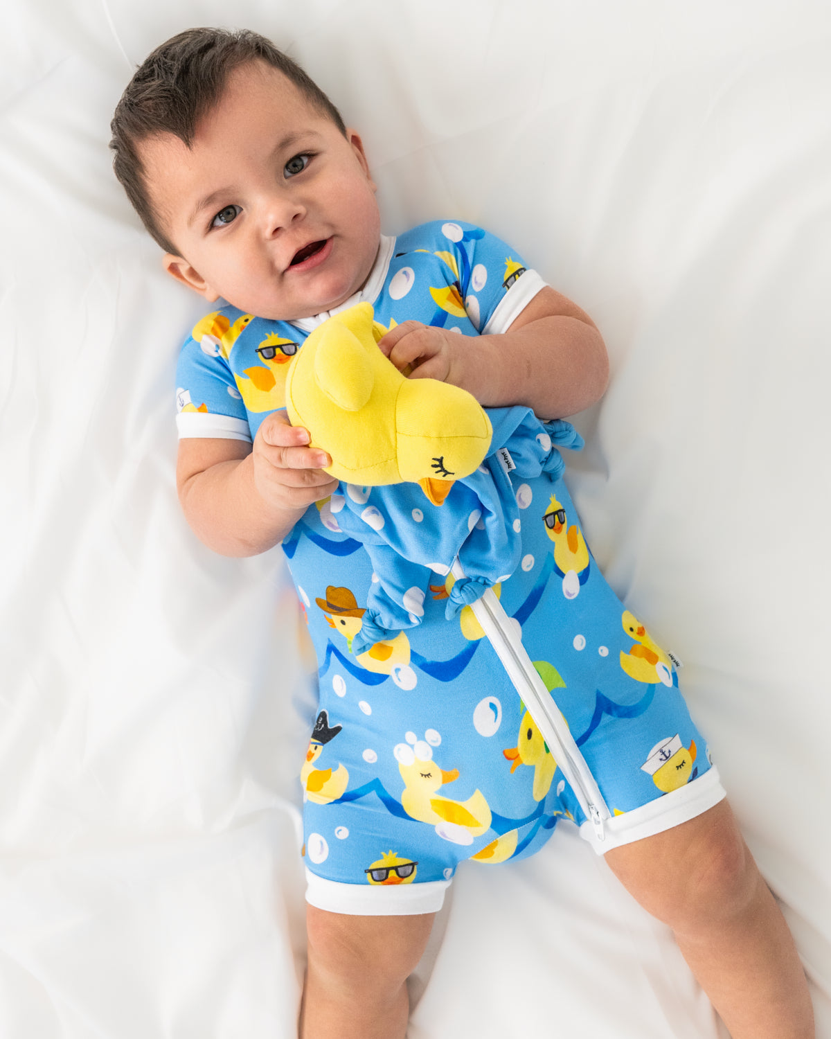 Aerial view of baby wearing the Splish Splash Shorty Zippy holding a rubber duck plush toy