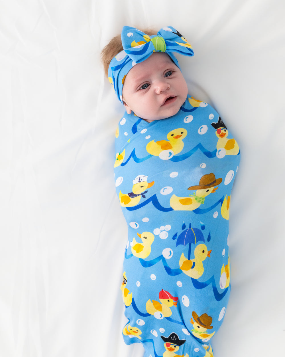 Aerial view of baby wearing the Splish Splash Swaddle & Luxe Bow Headband Set