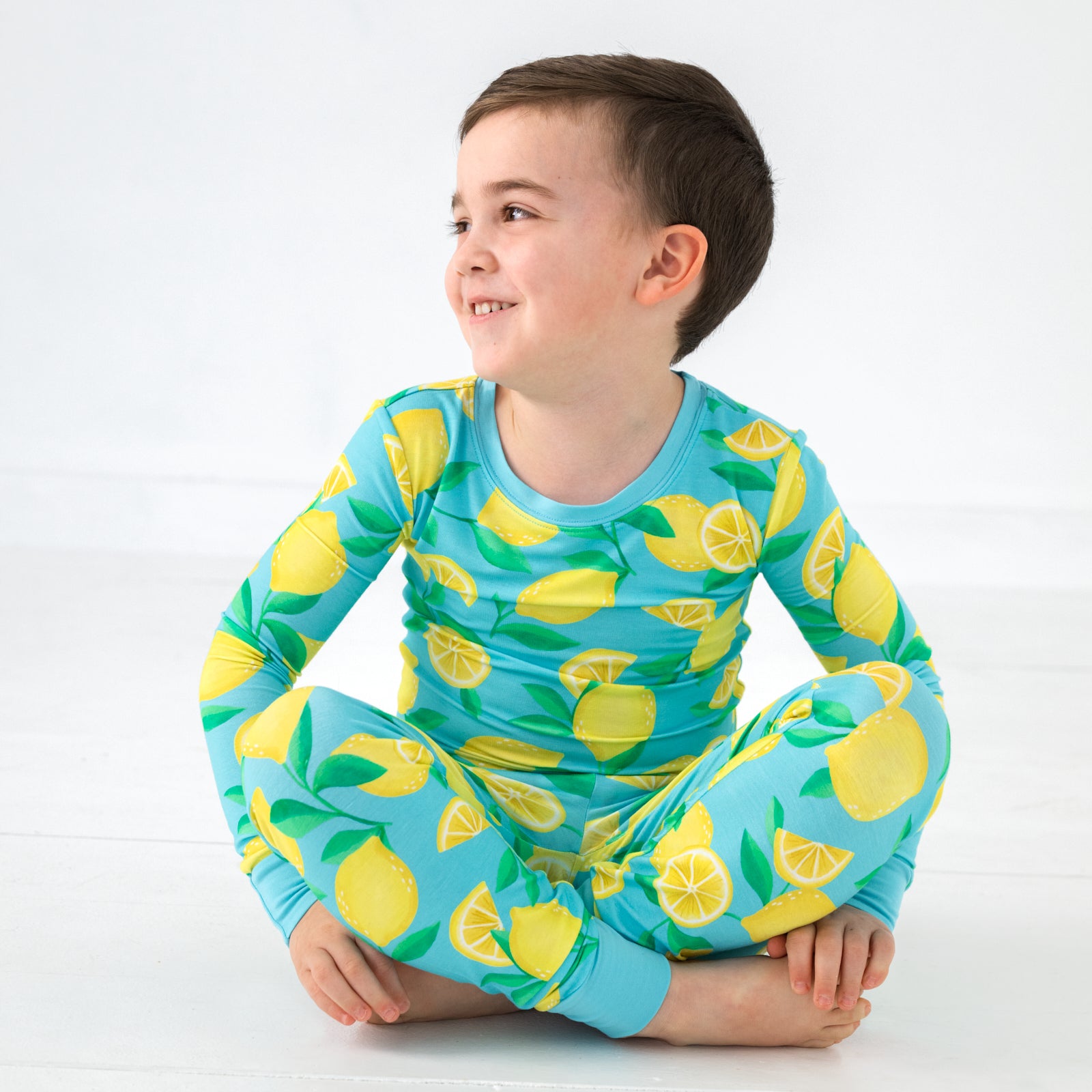 Sitting boy wearing the Blue Sunny Citrus Two-Piece Pajama Set
