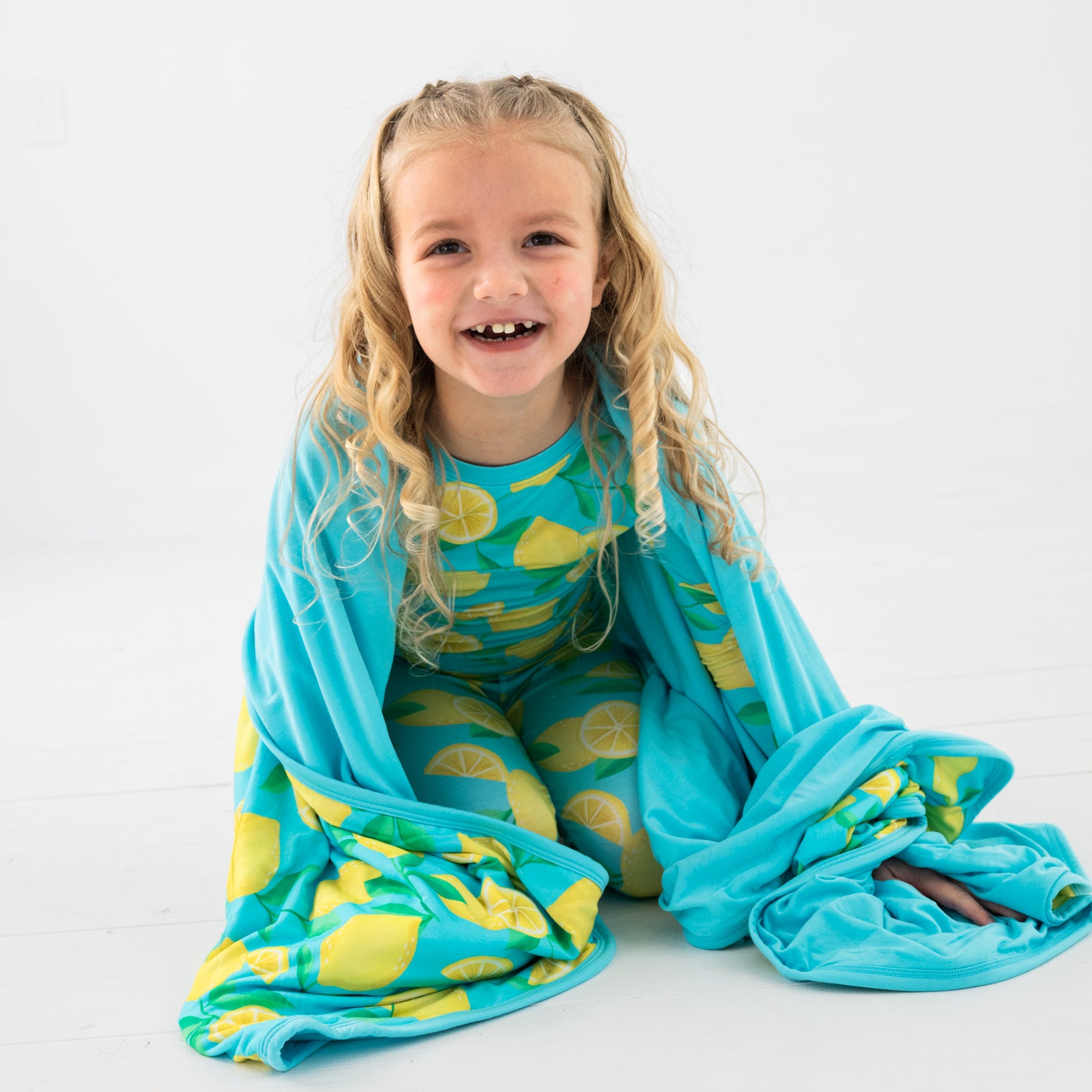 Sitting child wearing wrapped in the Blue Sunny Citrus Large Cloud Blanket®