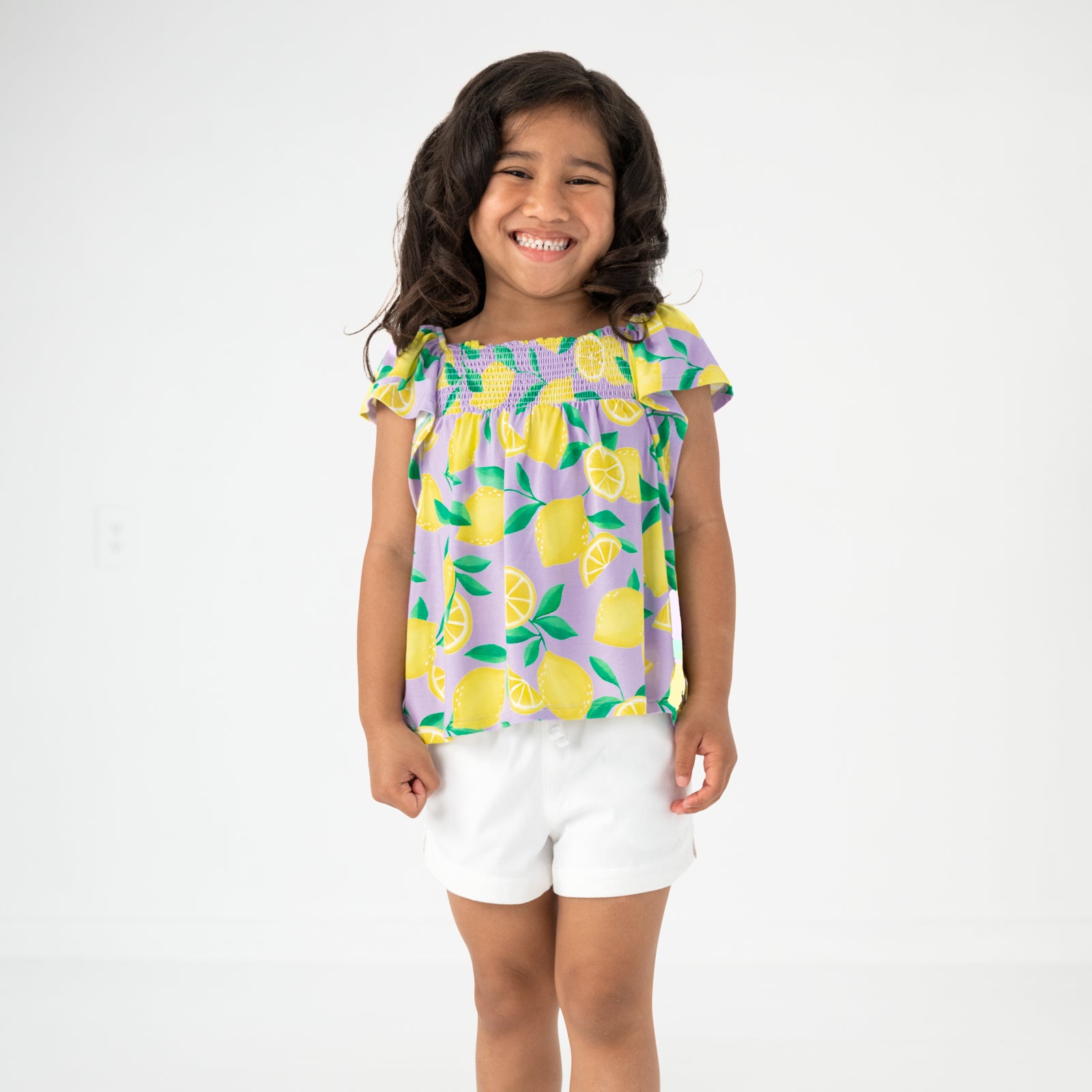Standing child wearing the Lavender Sunny Citrus Smocked Flutter Top