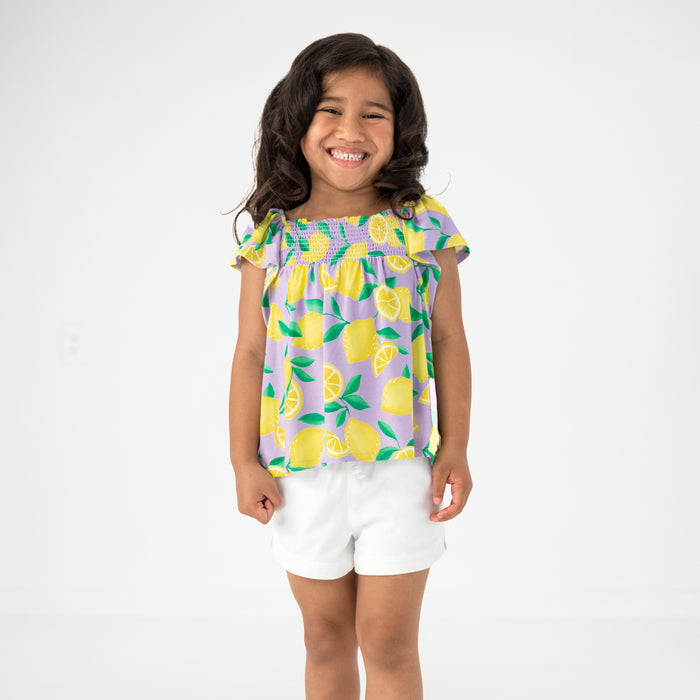Standing child wearing the Lavender Sunny Citrus Smocked Flutter Top