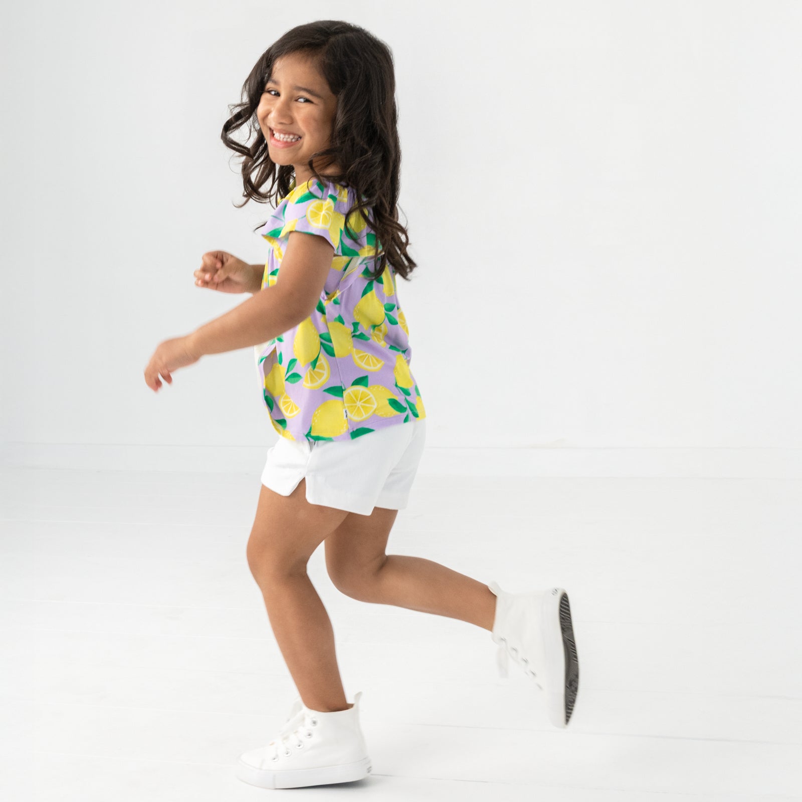 Running child wearing the Lavender Sunny Citrus Smocked Flutter Top with white denim shorts