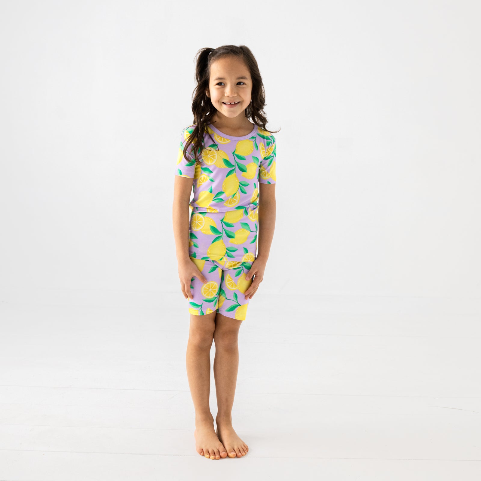 Standing child wearing the Lavender Sunny Citrus Two-Piece Short Sleeve & Shorts Pajama Set