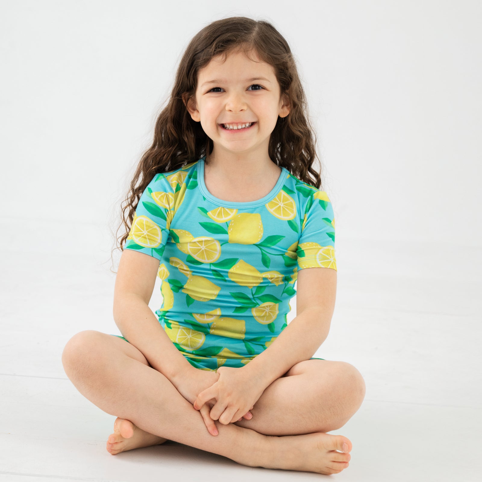 Sitting child wearing the Blue Sunny Citrus Two-Piece Short Sleeve & Shorts Pajama Set