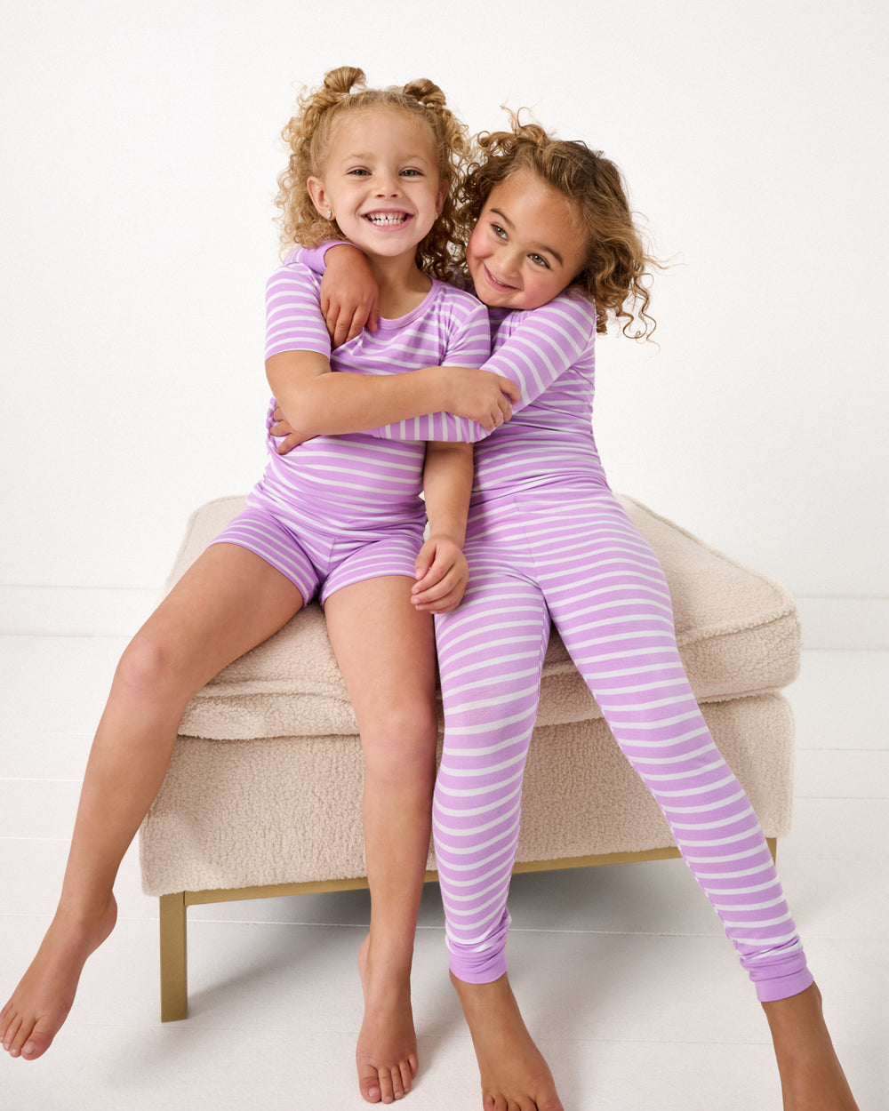 Two girls sitting on an ottoman wearing matching Sweet Orchid Stripe Two-Piece Pajama Sets