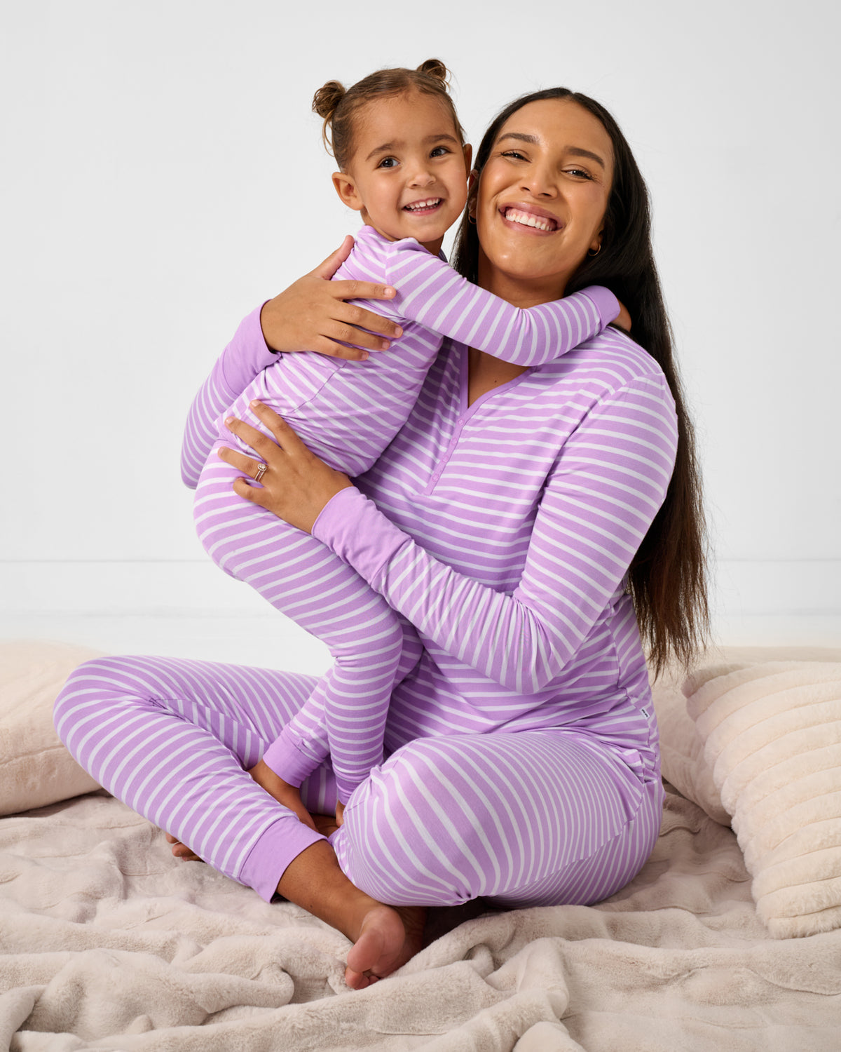 Mother and daughter wearing matching Sweet Orchid Stripe pajamas on a plush blanket