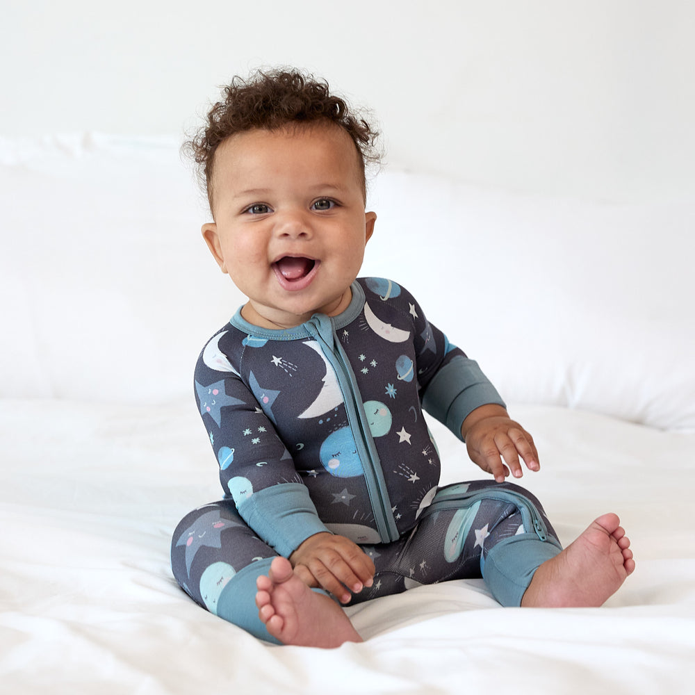 baby smiling sitting on bed wearing blue to the moon & back zippy