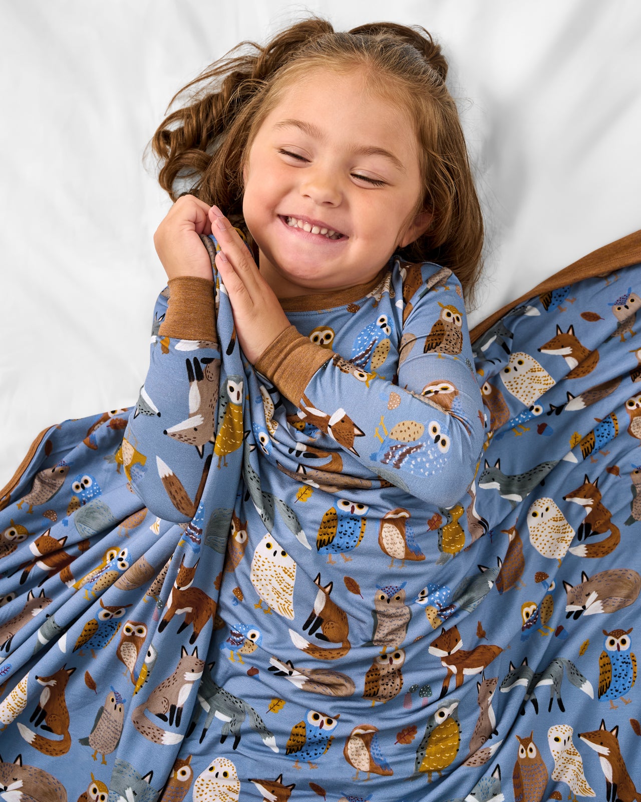 Girl snugged with the Twilight Pals Large Cloud Blanket® on a white bed