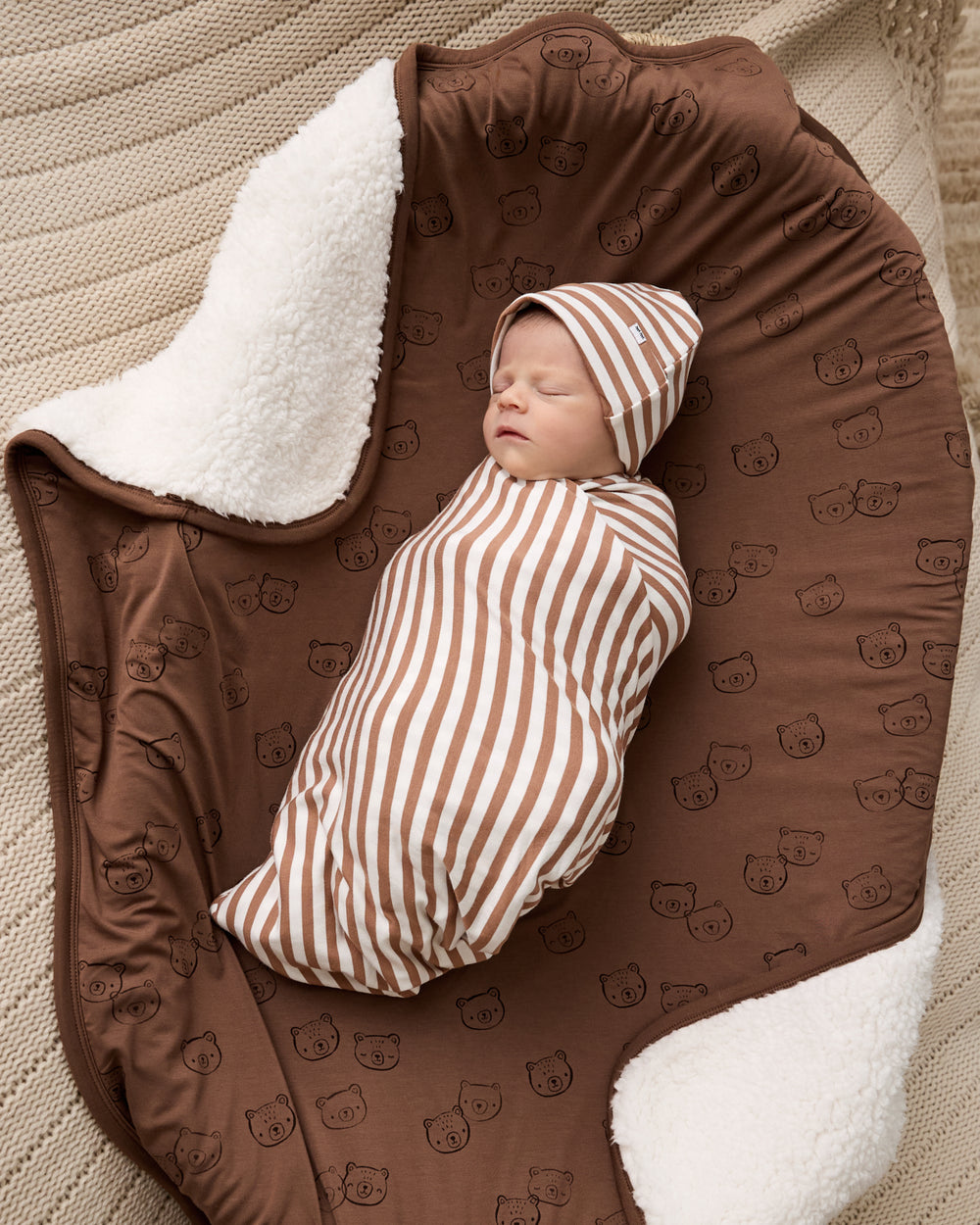 Newborn wrapped in the Chestnut Brown Stripe Swaddle & Luxe Bow Headband Set on the Teddy Tracks sherpa blanket