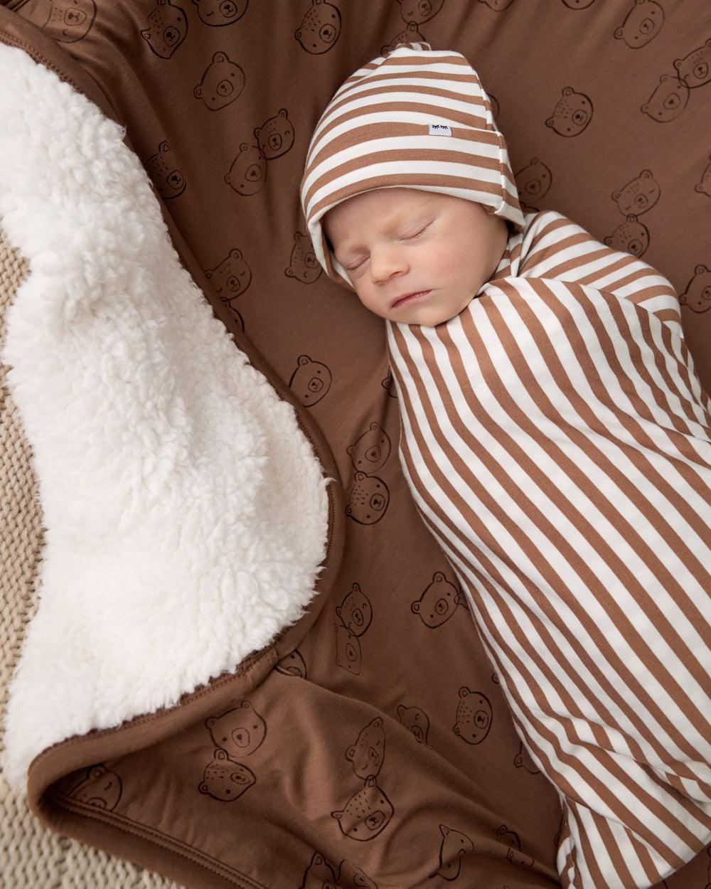 Aerial view of newborn in a striped swaddle laying on the Teddy Tracks Mini Cloud Blanket®