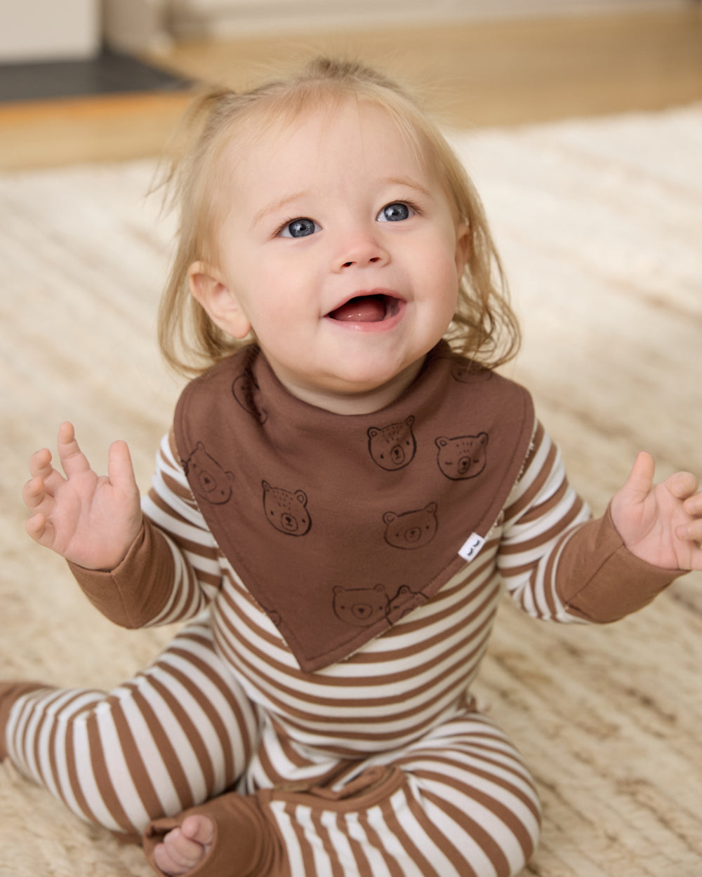 Sitting newborn wearing the Teddy Tracks Bandana Bib with a striped zippy