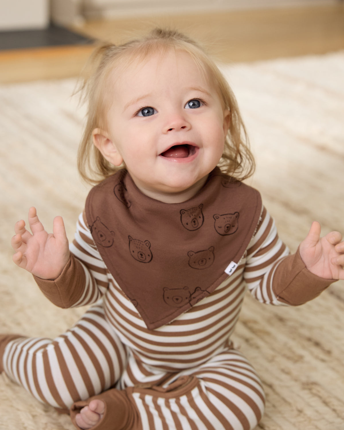 Sitting newborn wearing the Teddy Tracks Bandana Bib with a striped zippy