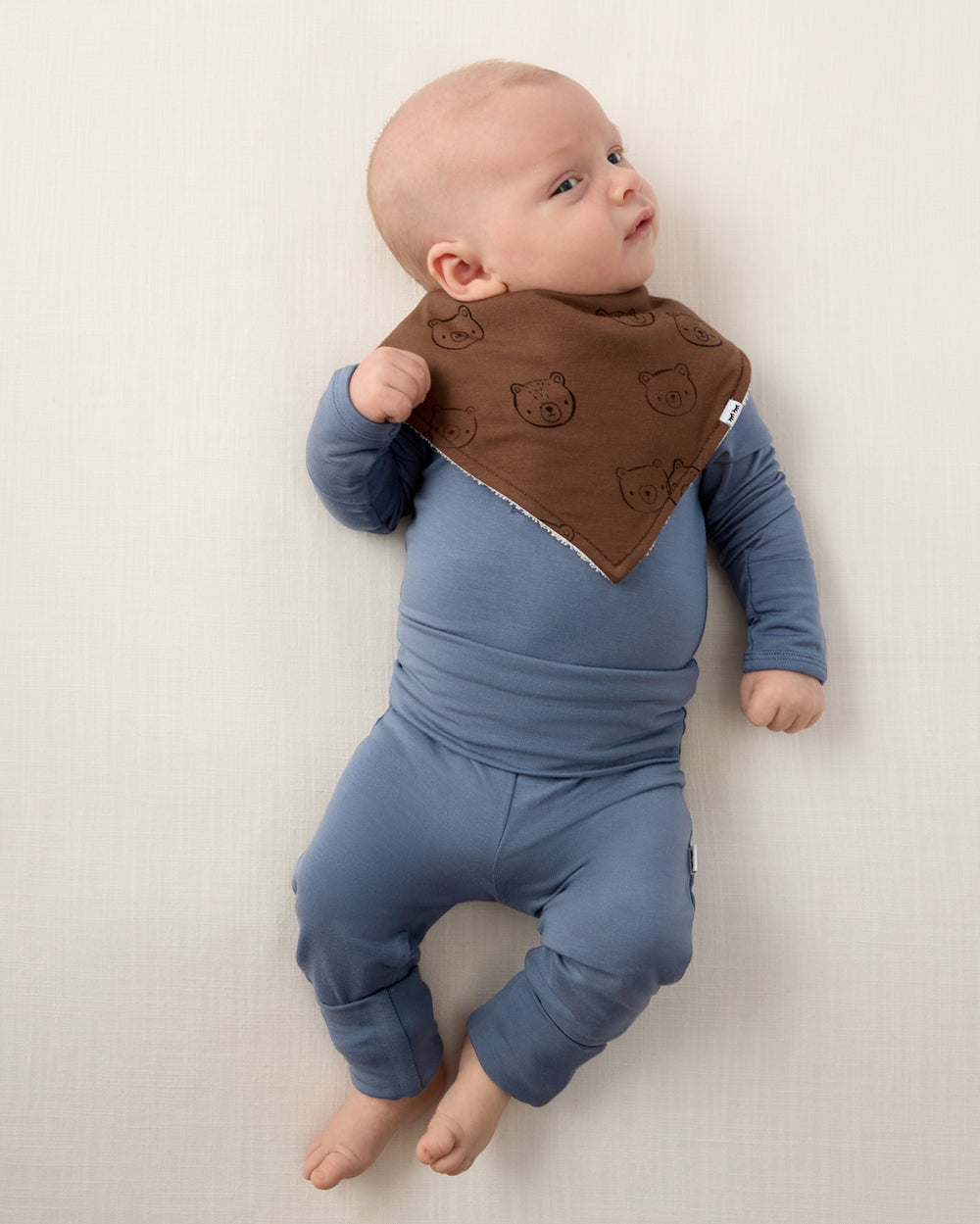 Aerial view of baby boy wearing the Teddy Tracks Bandana Bib with a blue newborn outfit