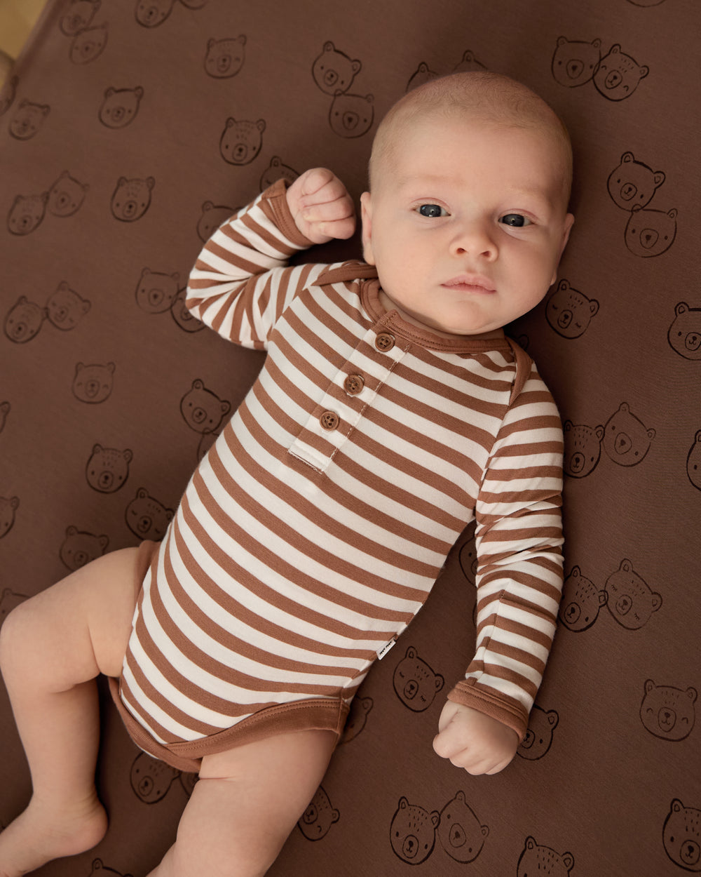 Aerial view of newborn wearing the Chestnut Brown Stripe Henley Bodysuit on a Teddy Tracks crib sheet