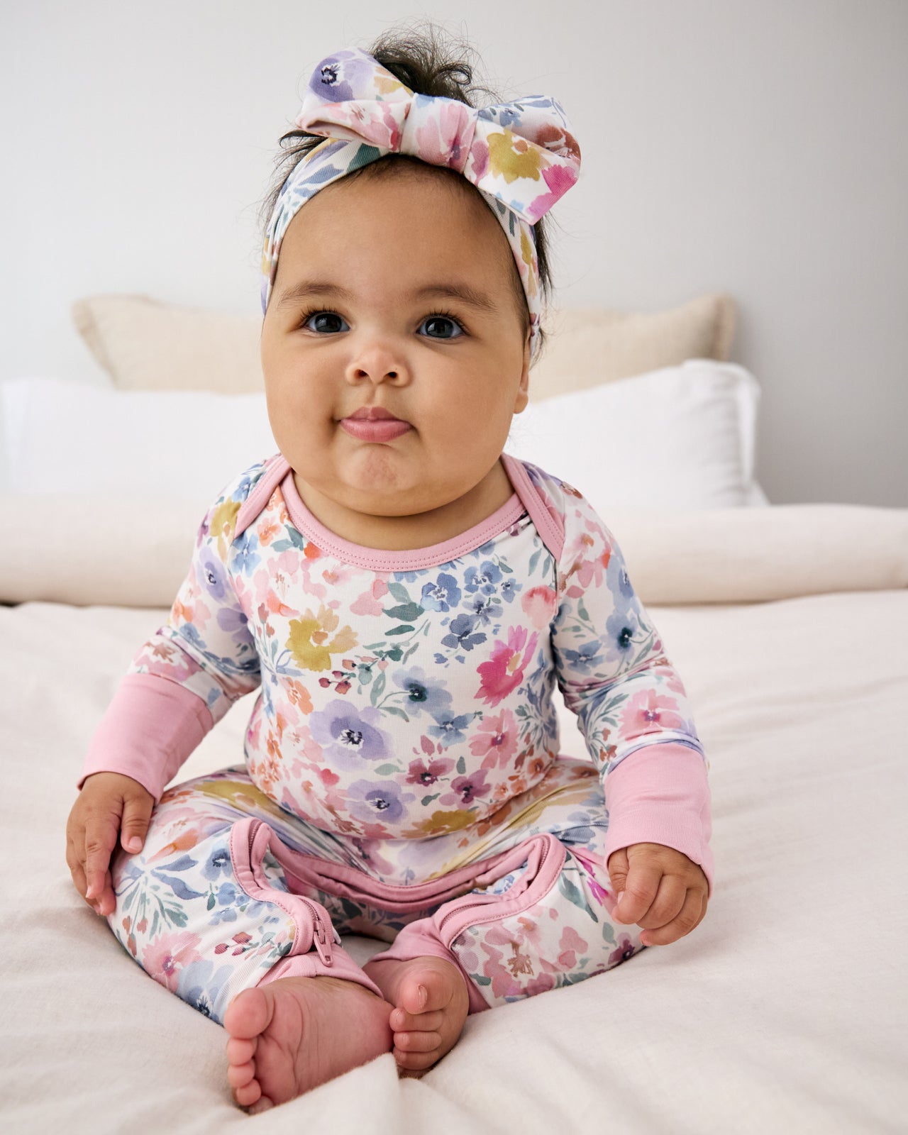 Sitting newborn wearing the Tiny Blooms Crescent Zippy with a matching luxe bow headband