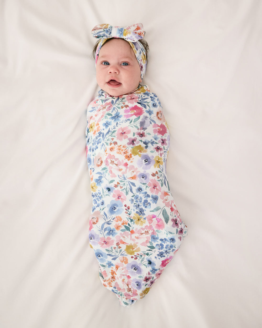 Aerial view of baby wearing the Tiny Blooms Swaddle & Luxe Bow Headband Set