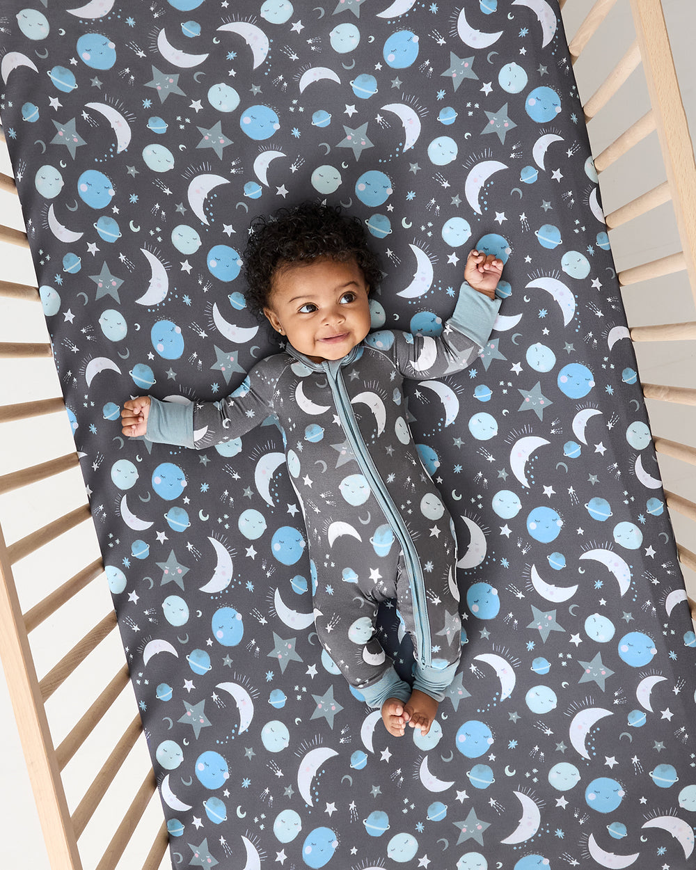 Overhead view of baby in a crib with the Blue To the Moon & Back Fitted Crib Sheet