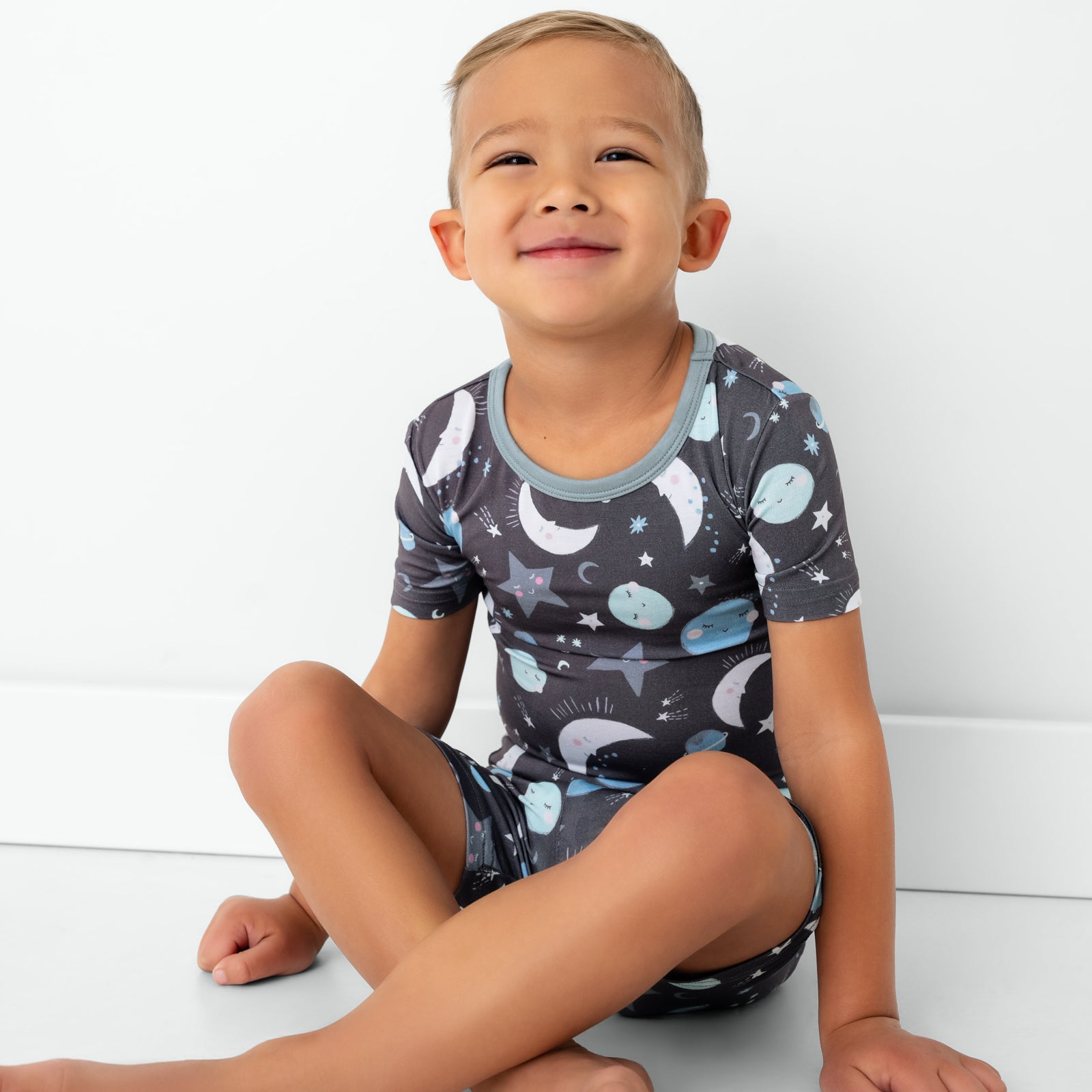 Sitting child wearing the Blue To the Moon & Back Two-Piece Short Sleeve & Shorts Pajama Set
