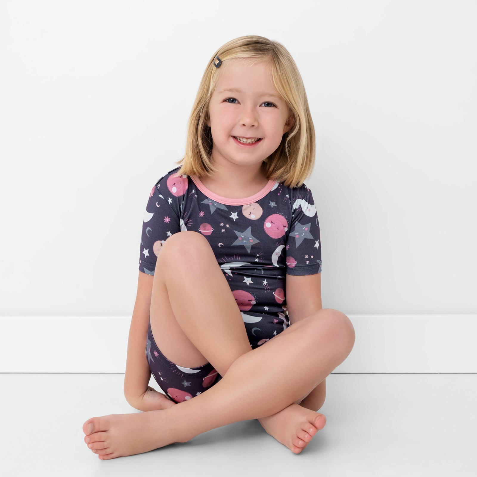 Sitting child wearing the Pink To the Moon & Back Two-Piece Short Sleeve & Shorts Pajama Set