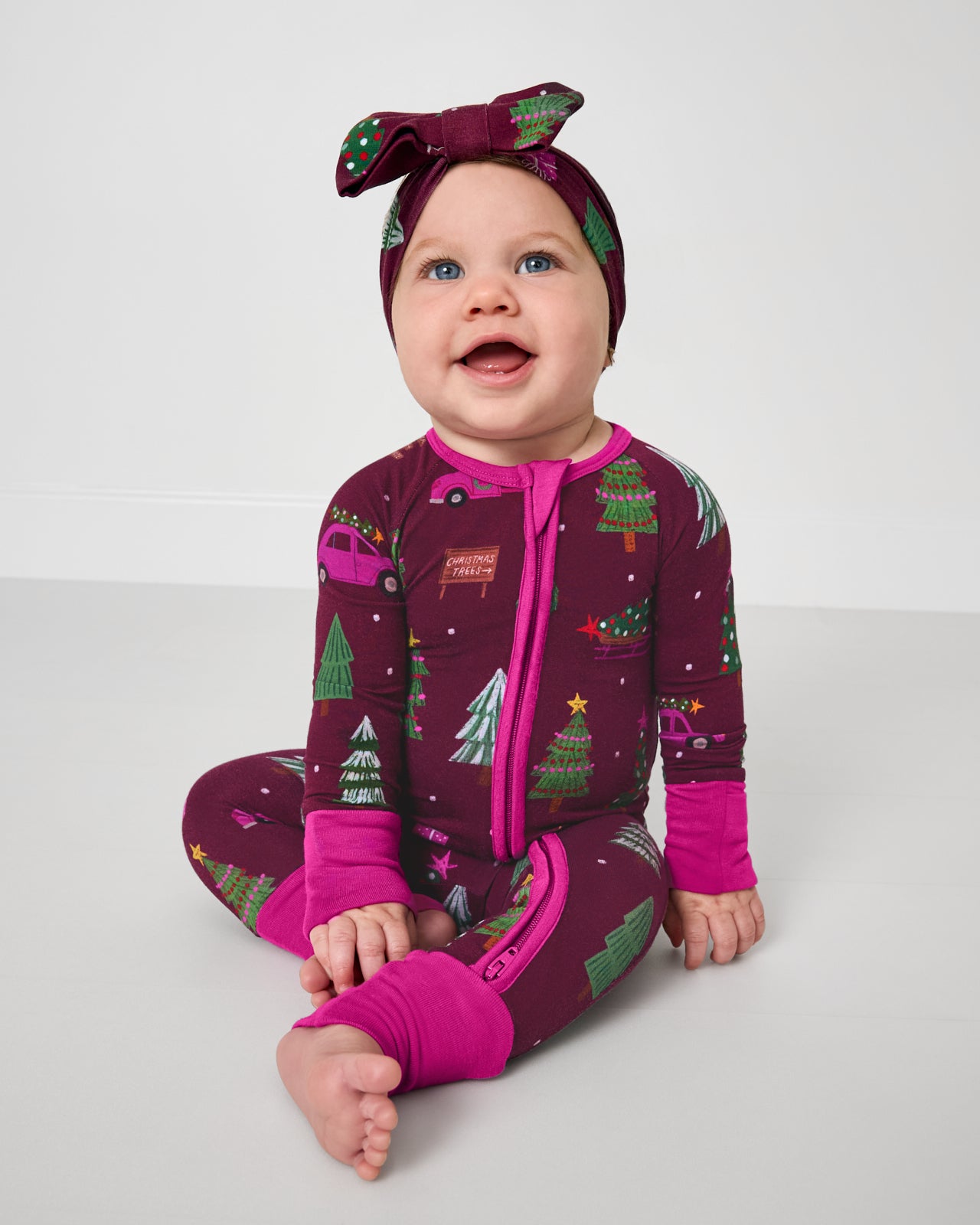 Sitting baby wearing the Cranberry Tree Traffic Zippy with a matching luxe bow headband
