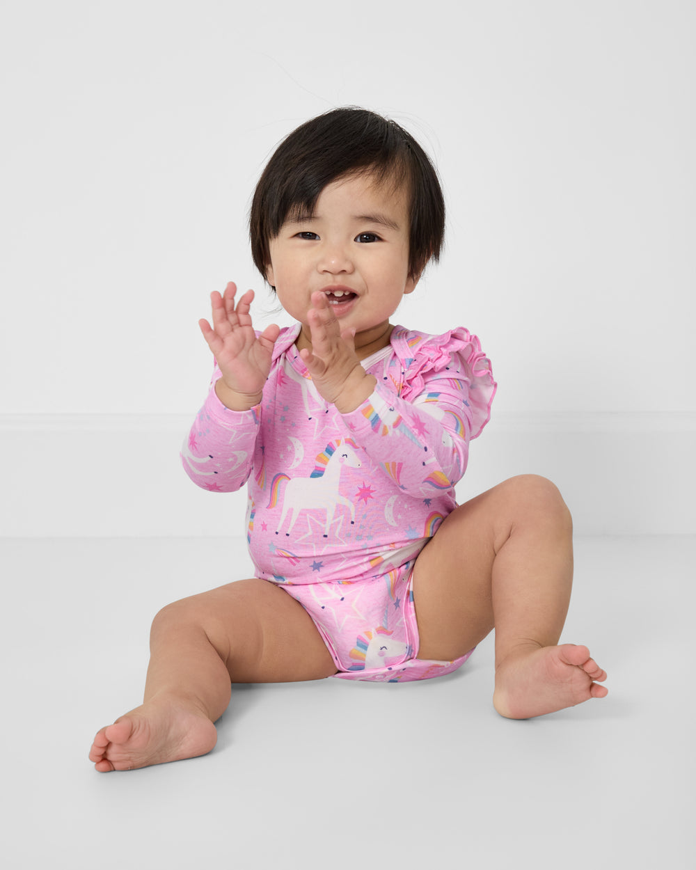 Clapping baby wearing the Unicorn Dance Flutter Bodysuit on a white background