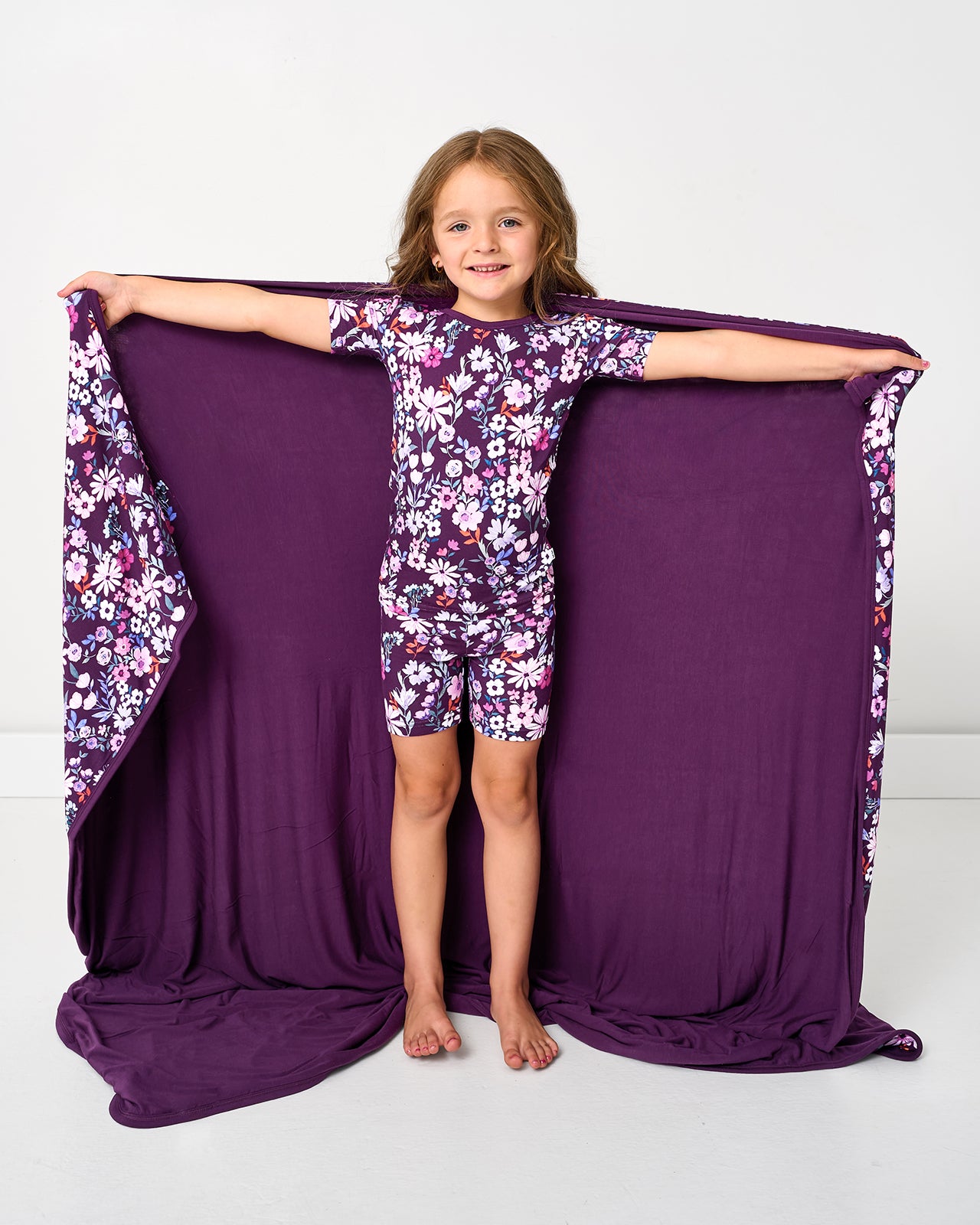 Standing girl holding up the Violet Meadow Large Cloud Blanket® to show the solid purple side