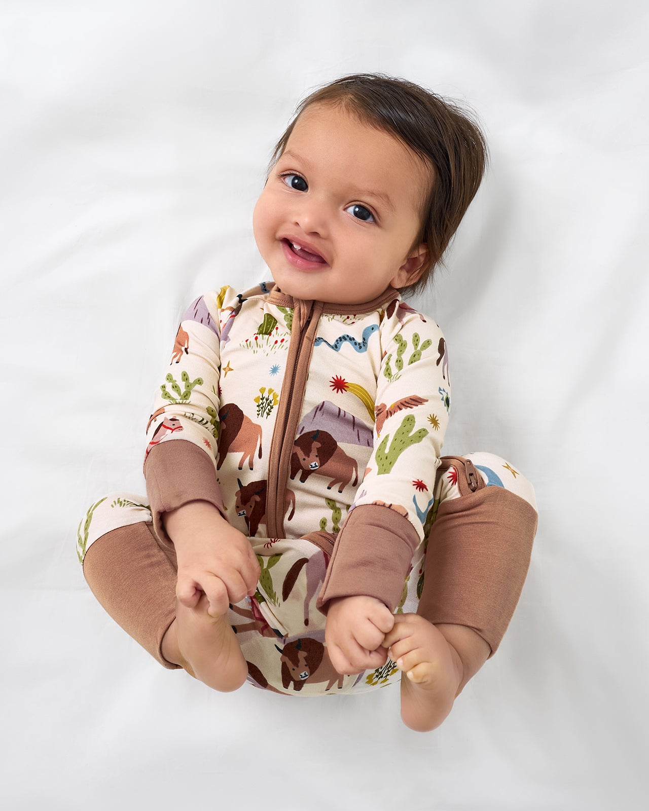 Baby laying on a white bed wearing the Wild Frontier Zippy