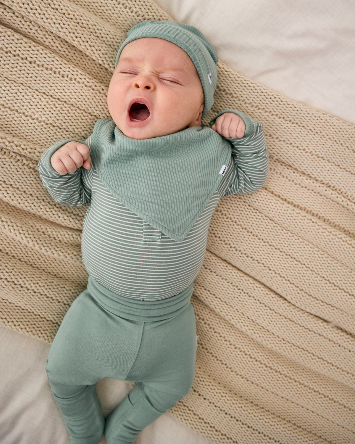 Aerial view of baby wearing the Willow Baby Ribbed Bandana Bib with matching sage green baby clothes