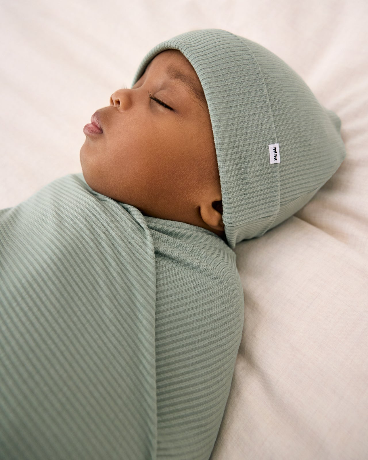 Close up of sleeping baby wearing the Willow Baby Ribbed Swaddle & Infant Beanie Set