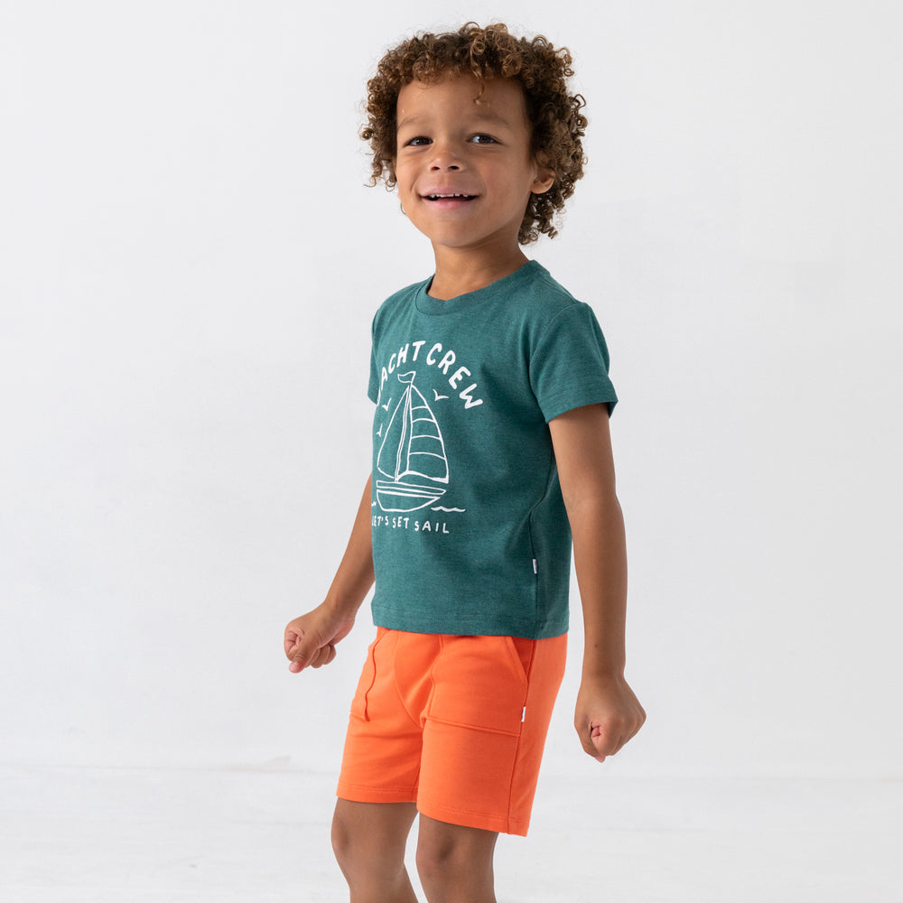 Standing child wearing the Yacht Crew Short Sleeve Relaxed Tee with coral shorts