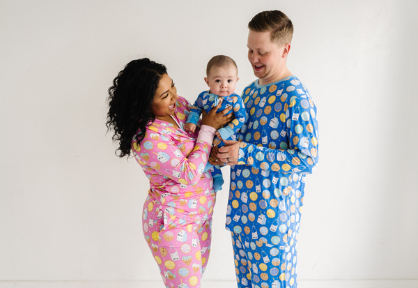 Family of three wearing matching pajamas on a plain background.