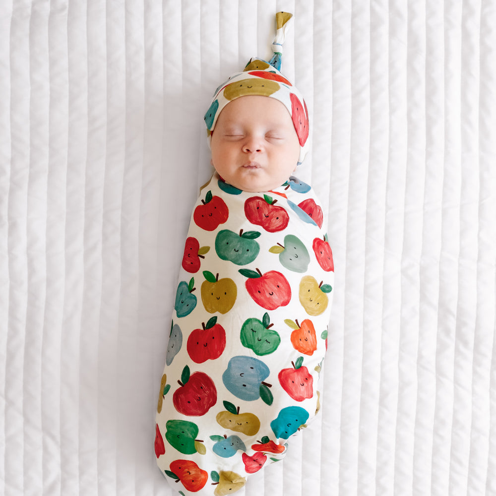 Child swaddled in a Red Apple of My Eye swaddle and hat set