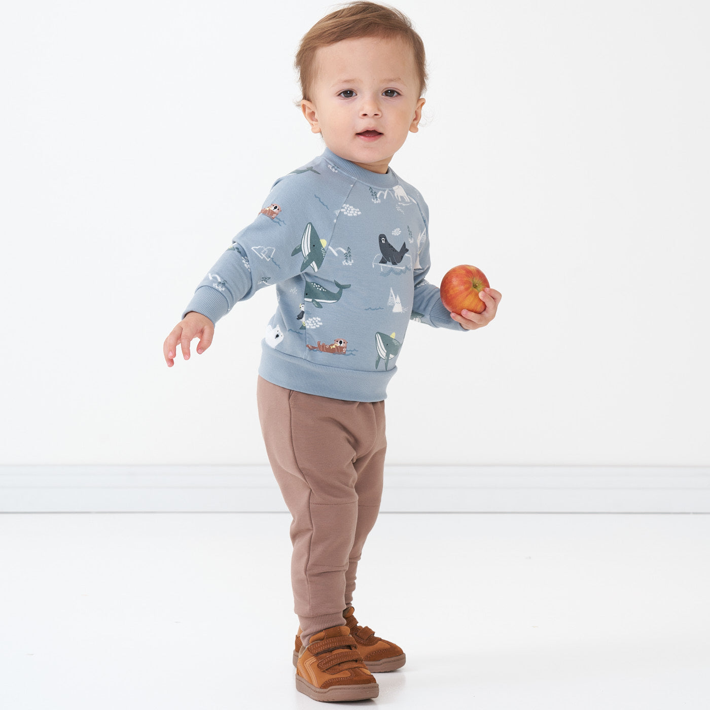Child holding an apple wearing an Arctic Animals printed crewneck sweatshirt and coordinating joggers