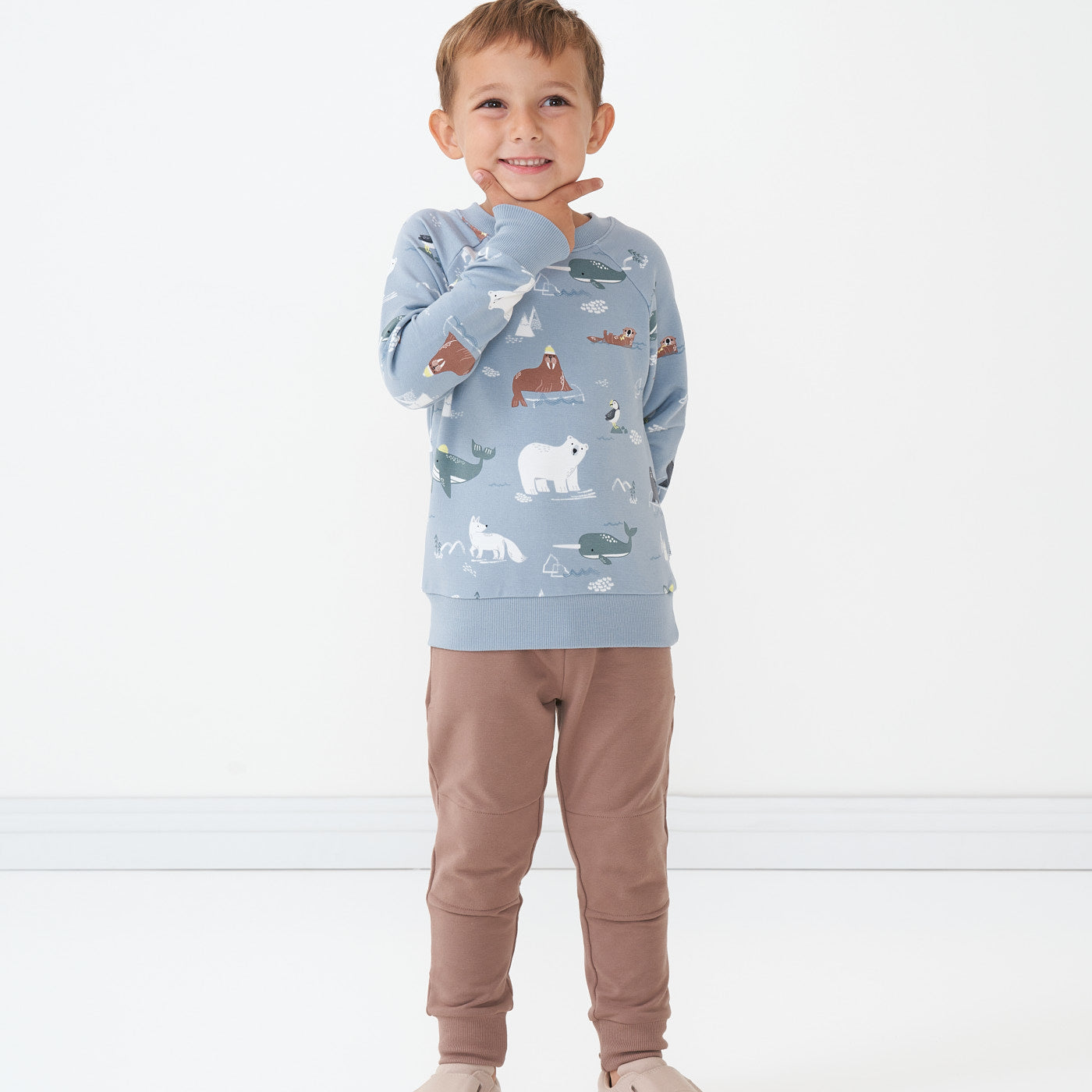 Child with his hand under his chin wearing an Arctic Animals printed crewneck sweatshirt and coordinating joggers