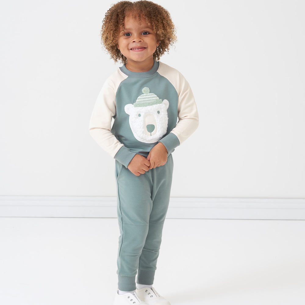 Child holding their hands together wearing a Polar Bear crewneck sweatshirt and coordinating Vintage Teal joggers