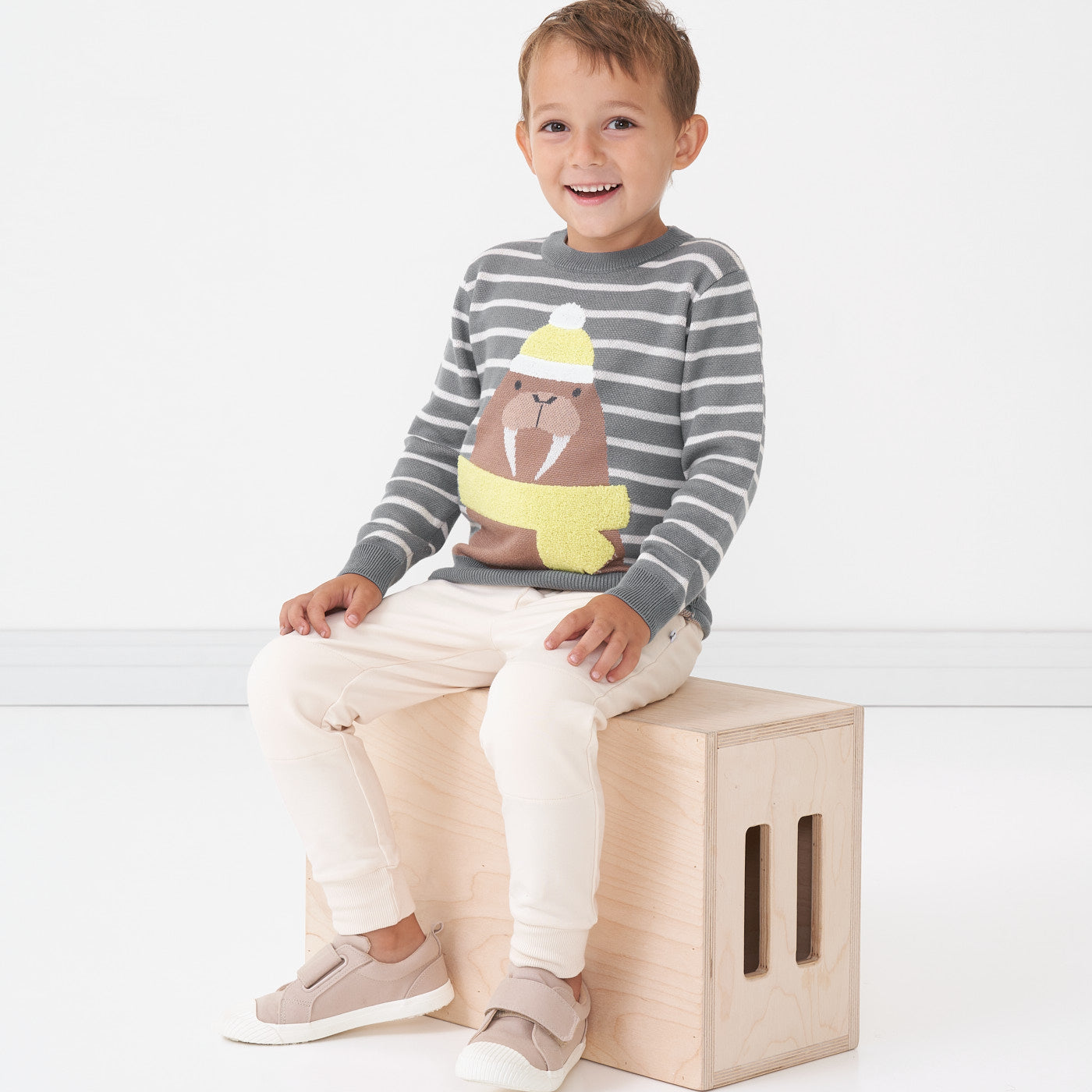 Child sitting on a box wearing a Walrus knit sweater and coordinating Cream joggers