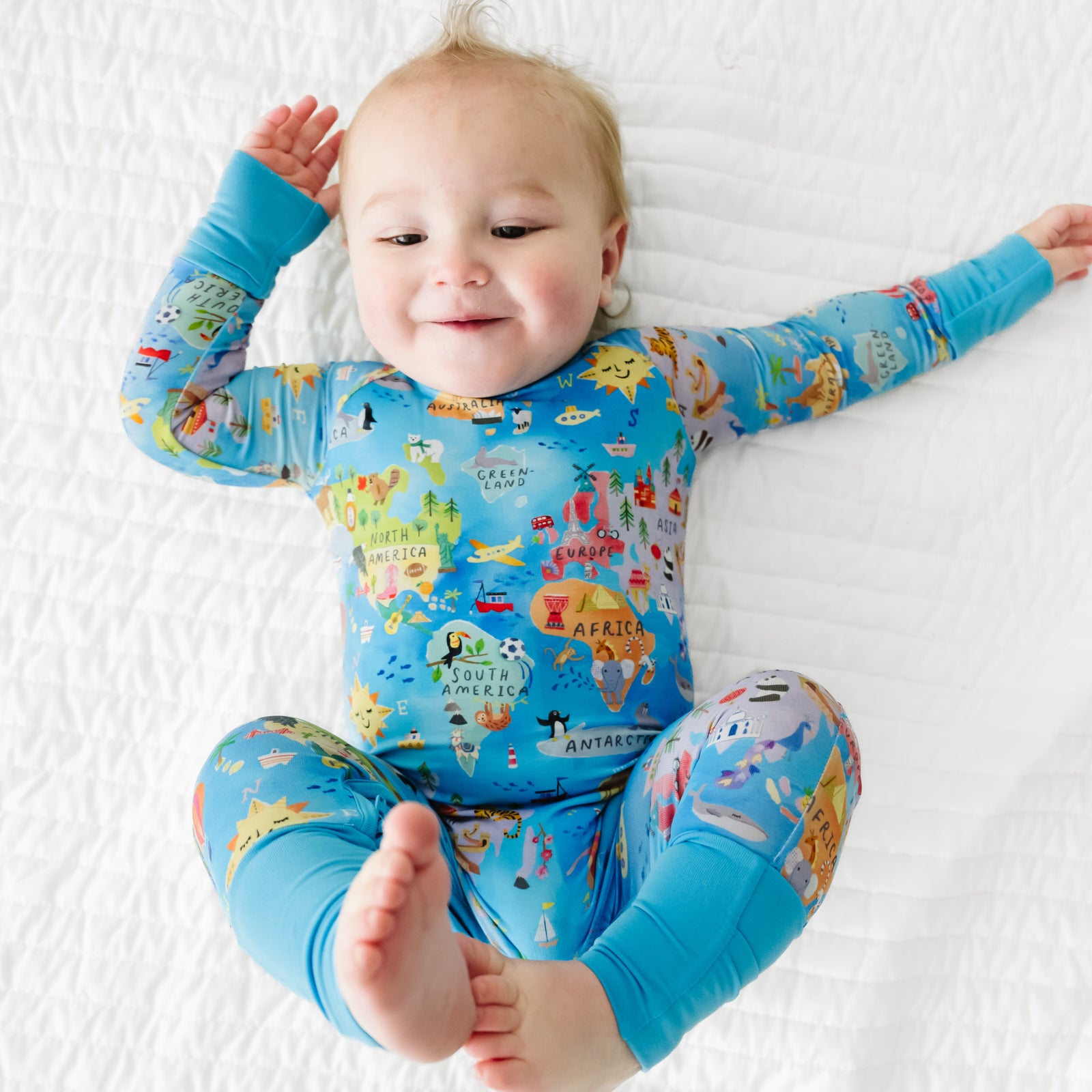 Smiling child lying on a bed wearing an Around the World crescent zippy