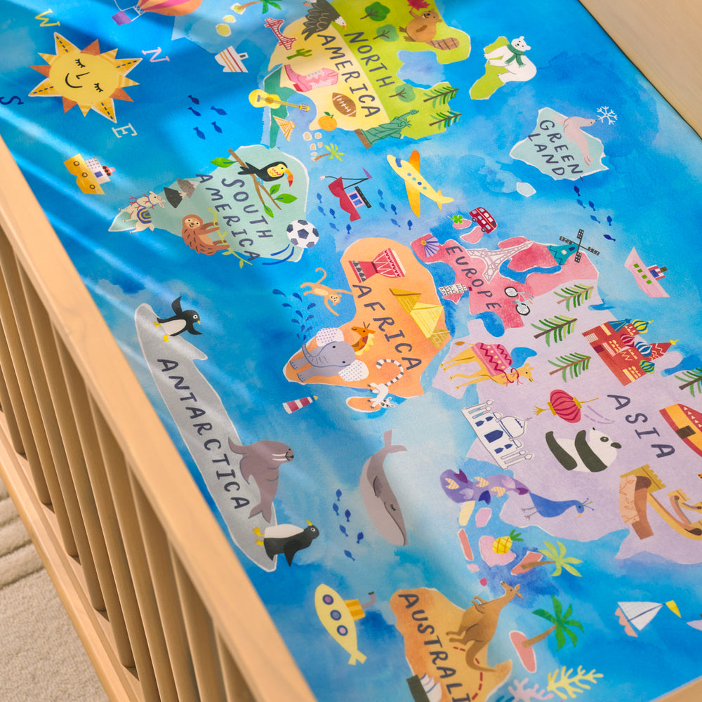 Close up view of an Around the World Fitted Crib Sheet on a mattress in a wooden crib