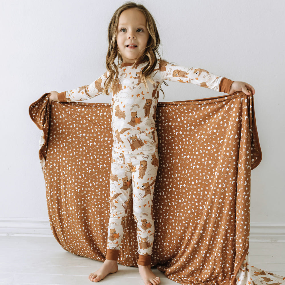 Child holding a Beary Sleepy Large Cloud Blanket out behind them showing the star and moon printed backing and wearing matching pajamas