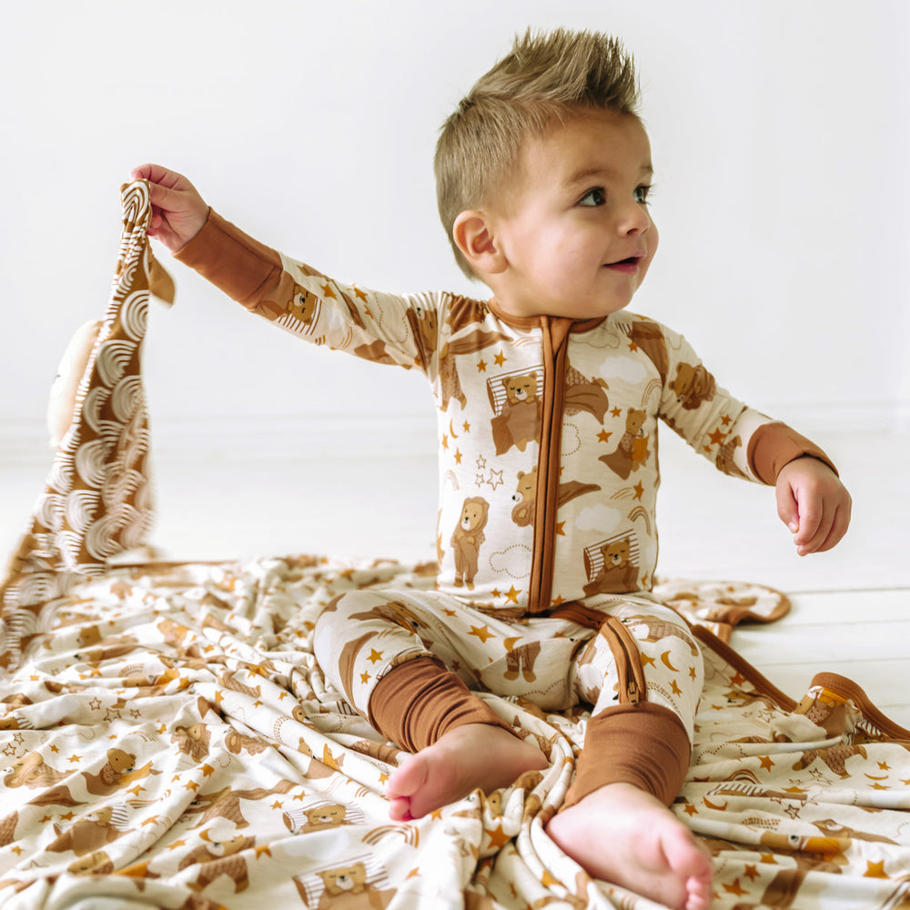 Child sitting on a Beary Sleepy Large Cloud Blanket and wearing a matching Zippy.