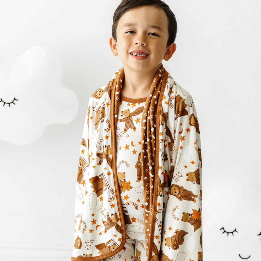 Close up view of a child with a Beary Sleepy Large Cloud Blanket draped over their shoulders and wearing matching pajamas.