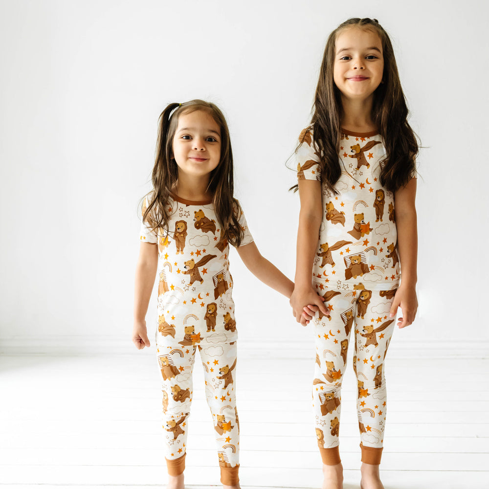 Two children holding hands and wearing matching Beary Sleepy Two-Piece Short Sleeve Pajama Sets.