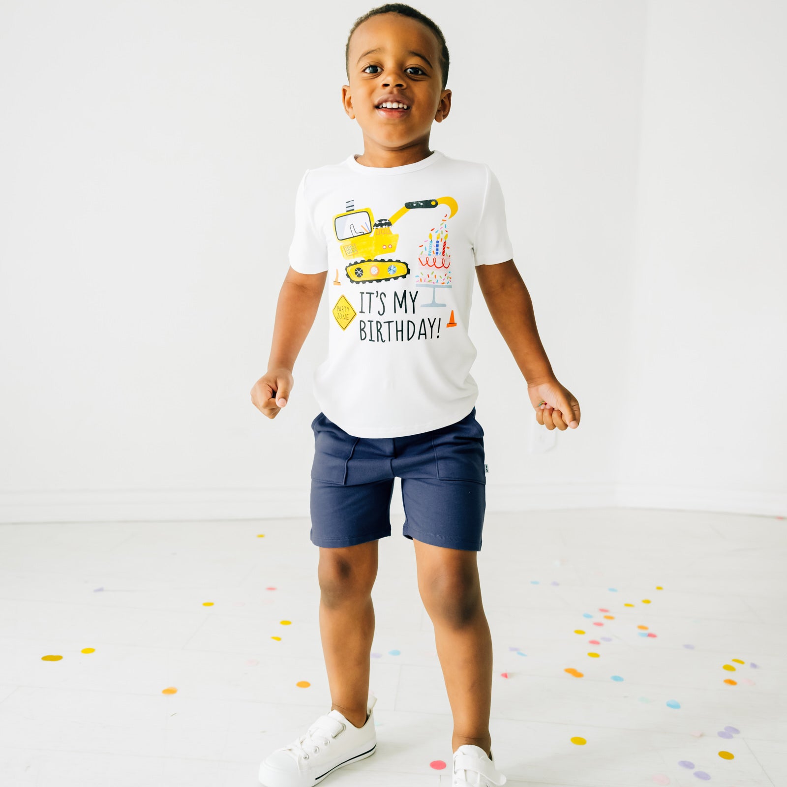 Child playing with confetti wearing a Birthday Builders Construction Graphic Tee paired with Vintage Navy Shorts