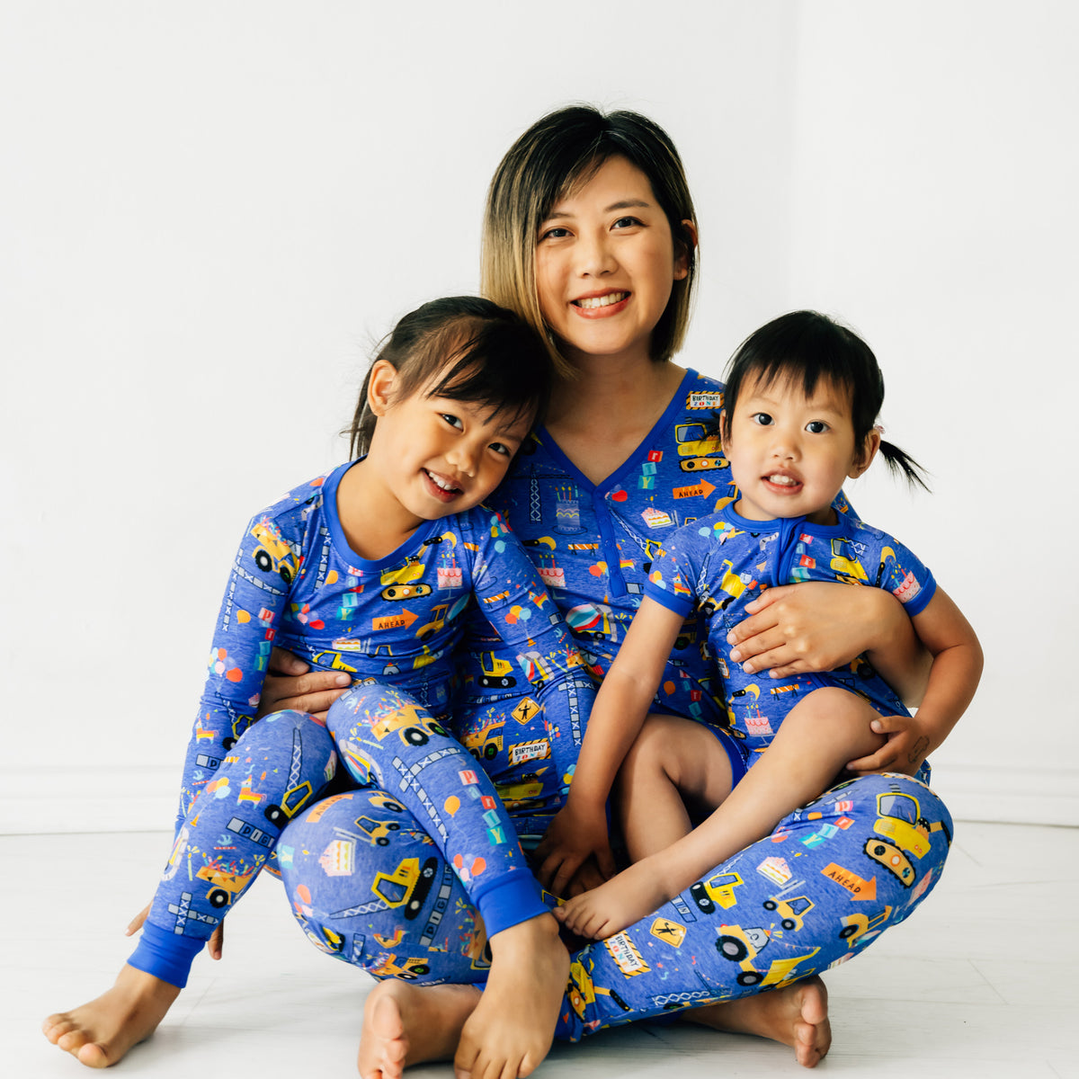 Mother and two children sitting on the ground wearing Birthday Builders mommy & me matching pajamas