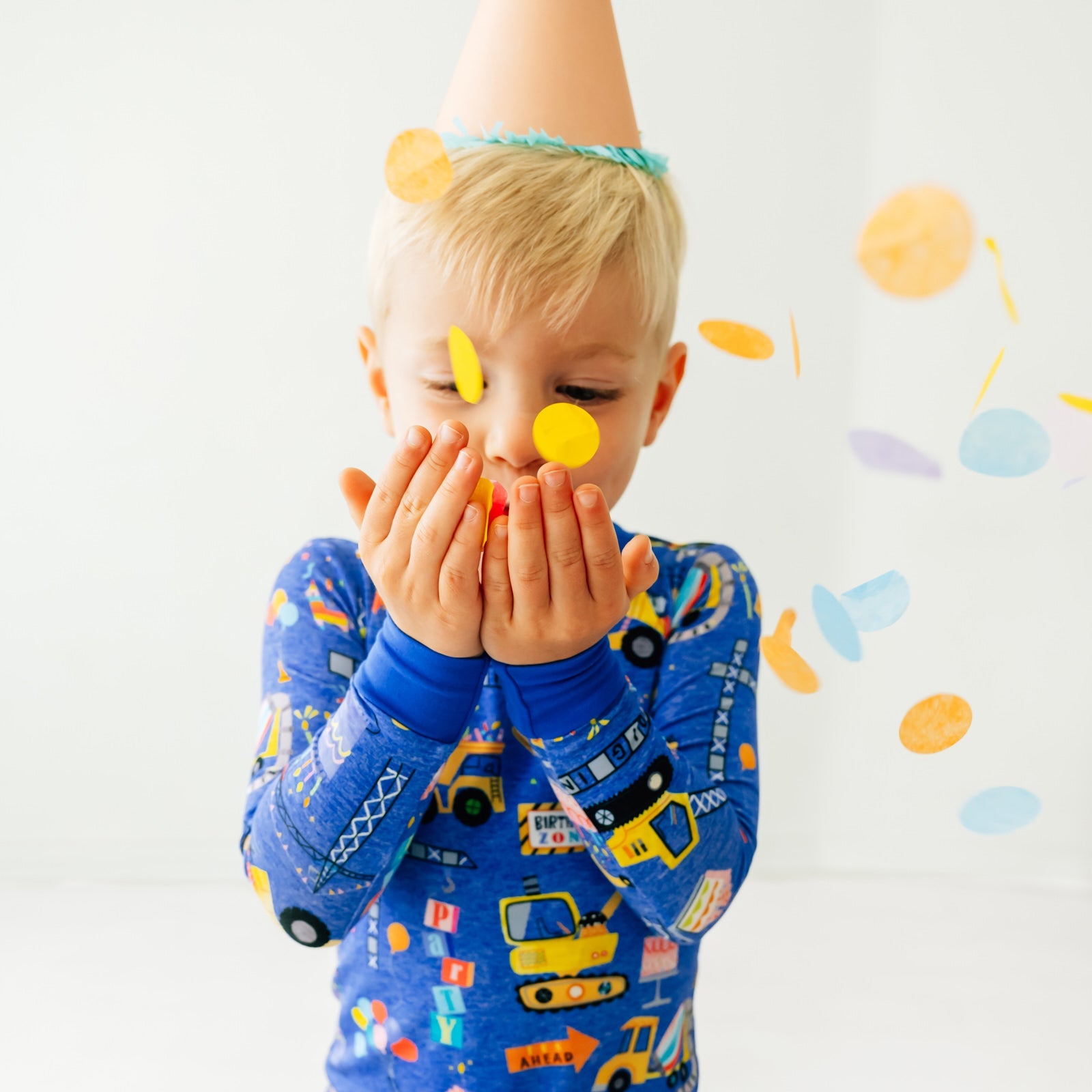 Close up of a child with a party hat on and playing with confetti wearing a Birthday Builders Two-Piece Pajama Set
