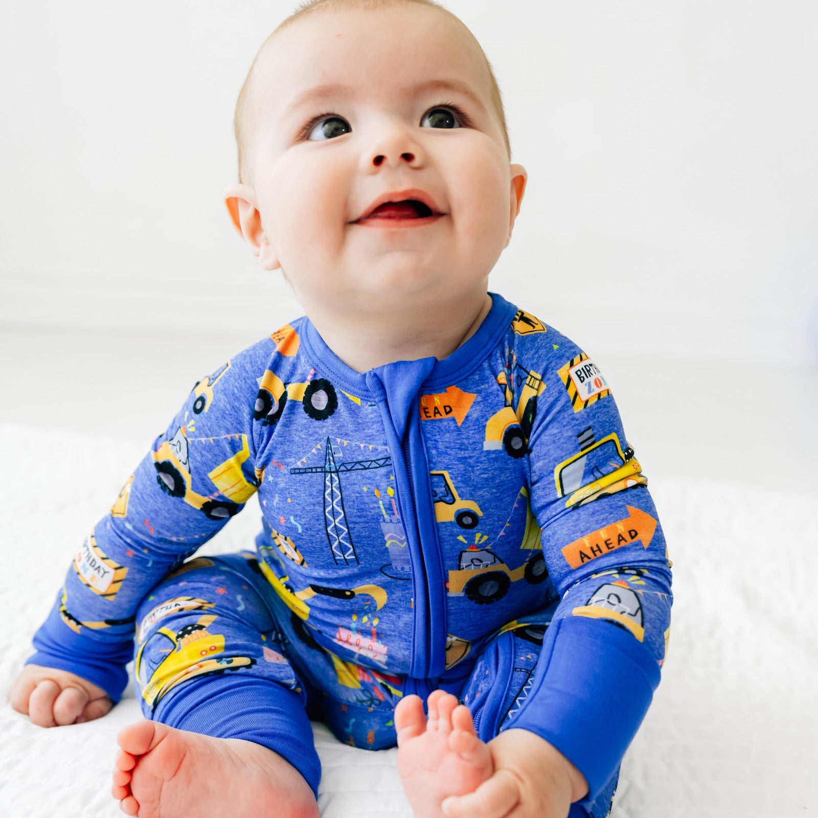 Close up of a child sitting on the ground wearing a Birthday Builders Zippy