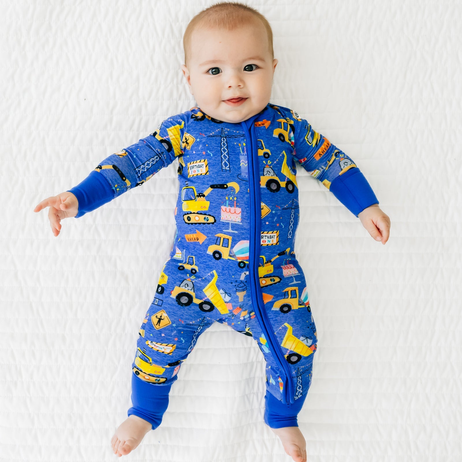 Infant lying down wearing a Birthday Builders Zippy