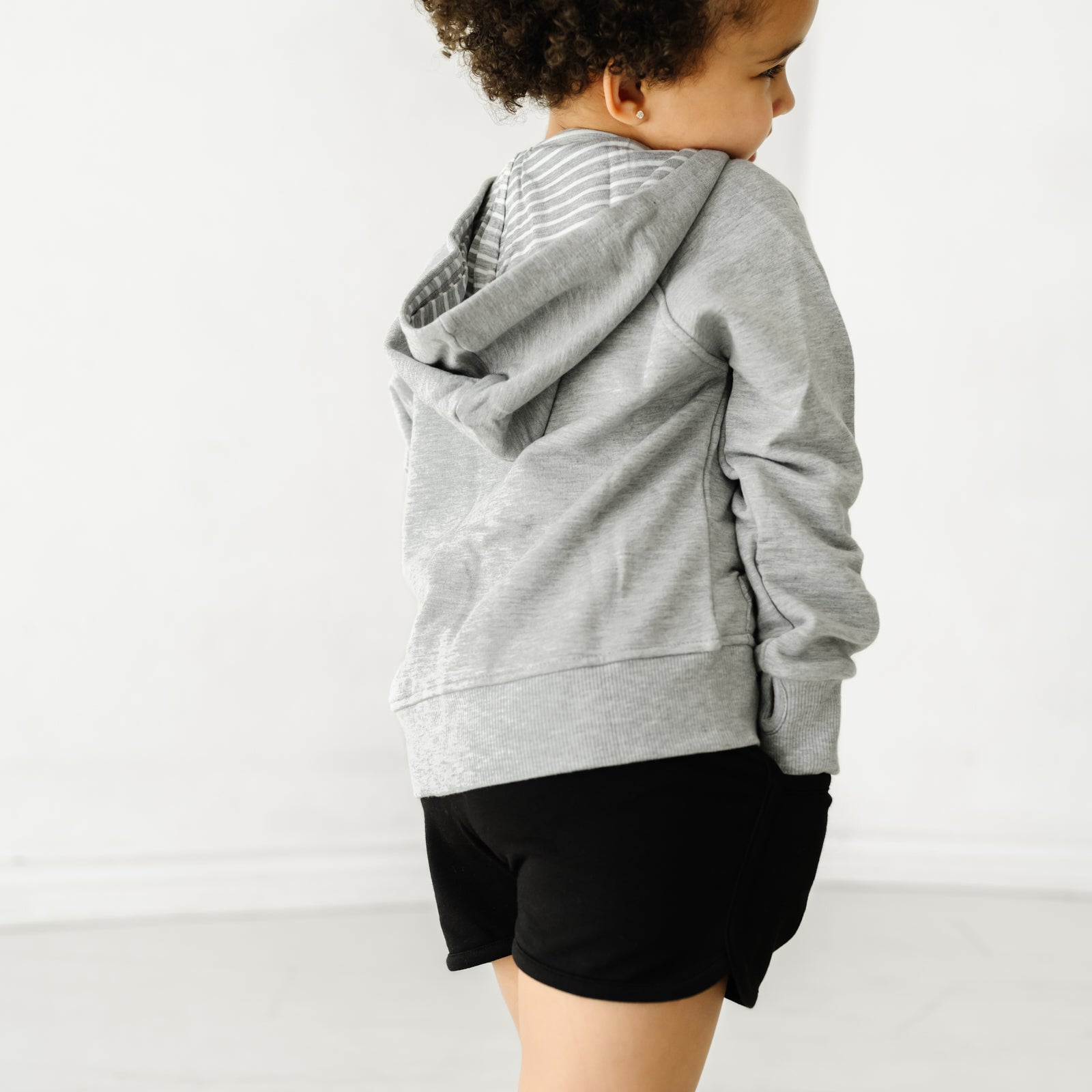 Back view of a child wearing Black Dolphin Shorts and coordinating light heather gray girls zip hoodie